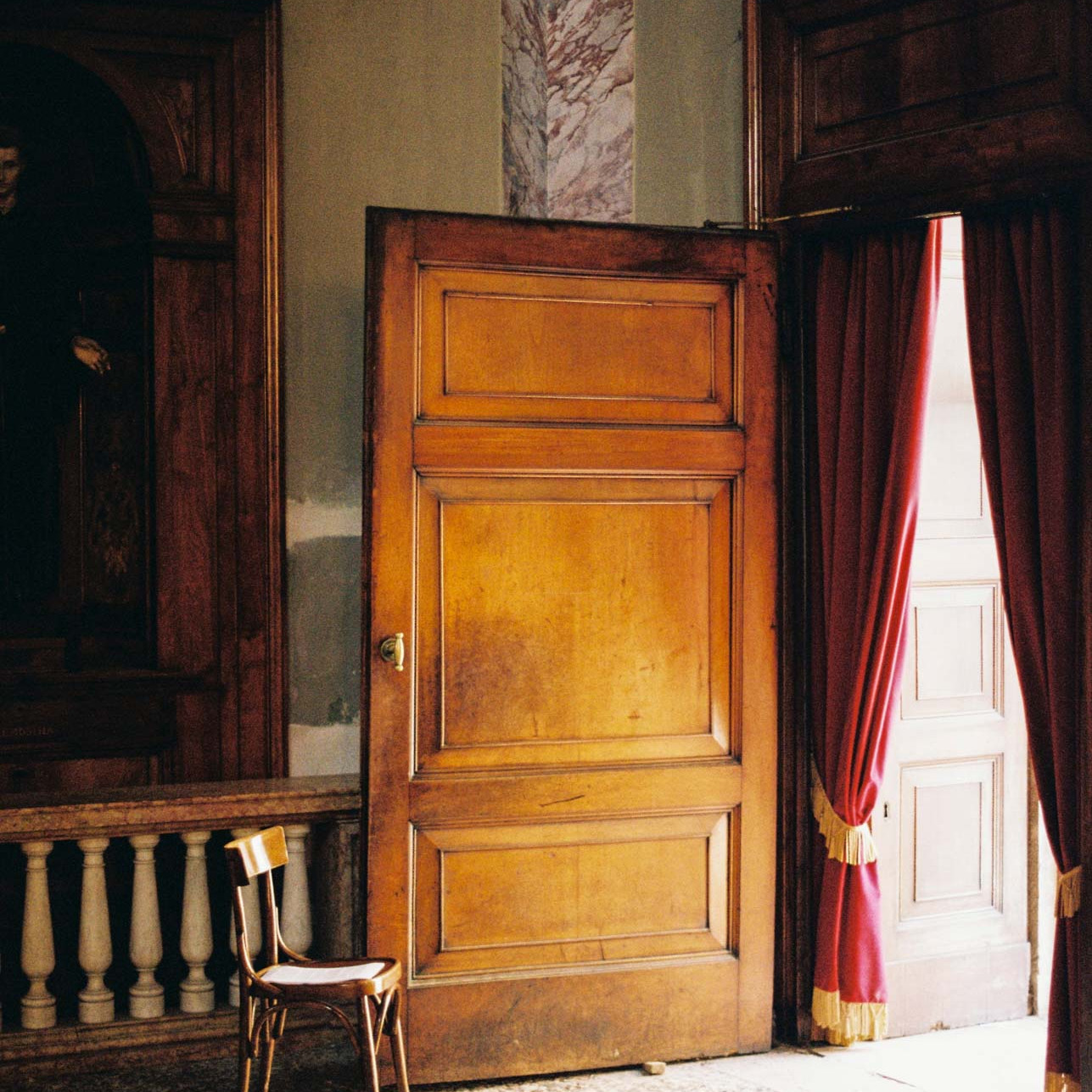 A large wooden door with light pouring through onto a chair in a chapel in citta alta, Bergamo, Italy taken on Kodak Gold 200