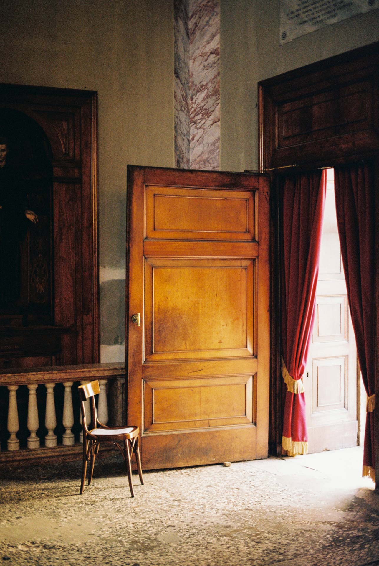 A large wooden door with light pouring through onto a chair in a chapel in citta alta, Bergamo, Italy taken on Kodak Gold 200
