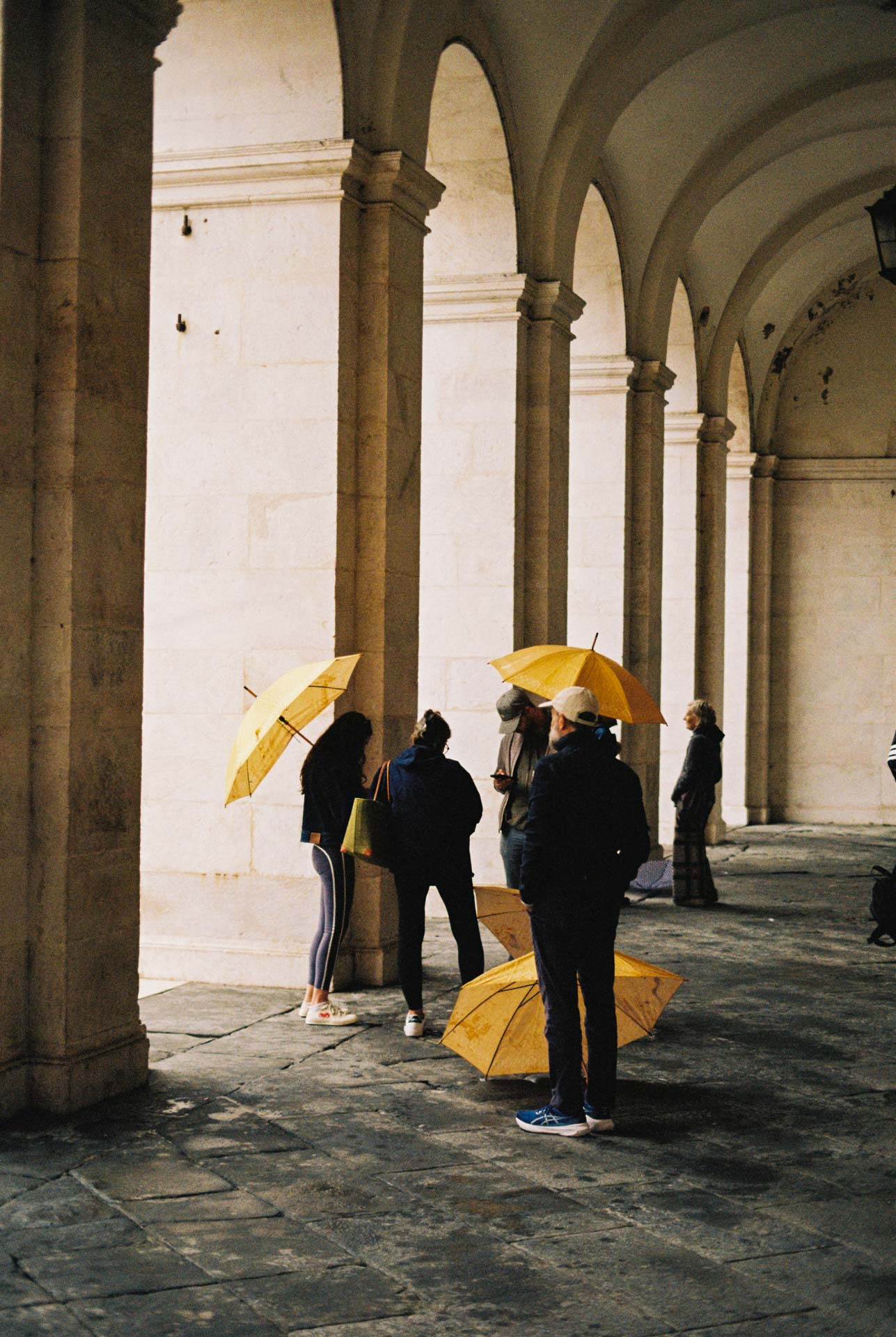 Tourists with yellow umbrellas stand underneath an arched alley in citta Alta, Bergamo, italy taken in Kodak Gold 200.