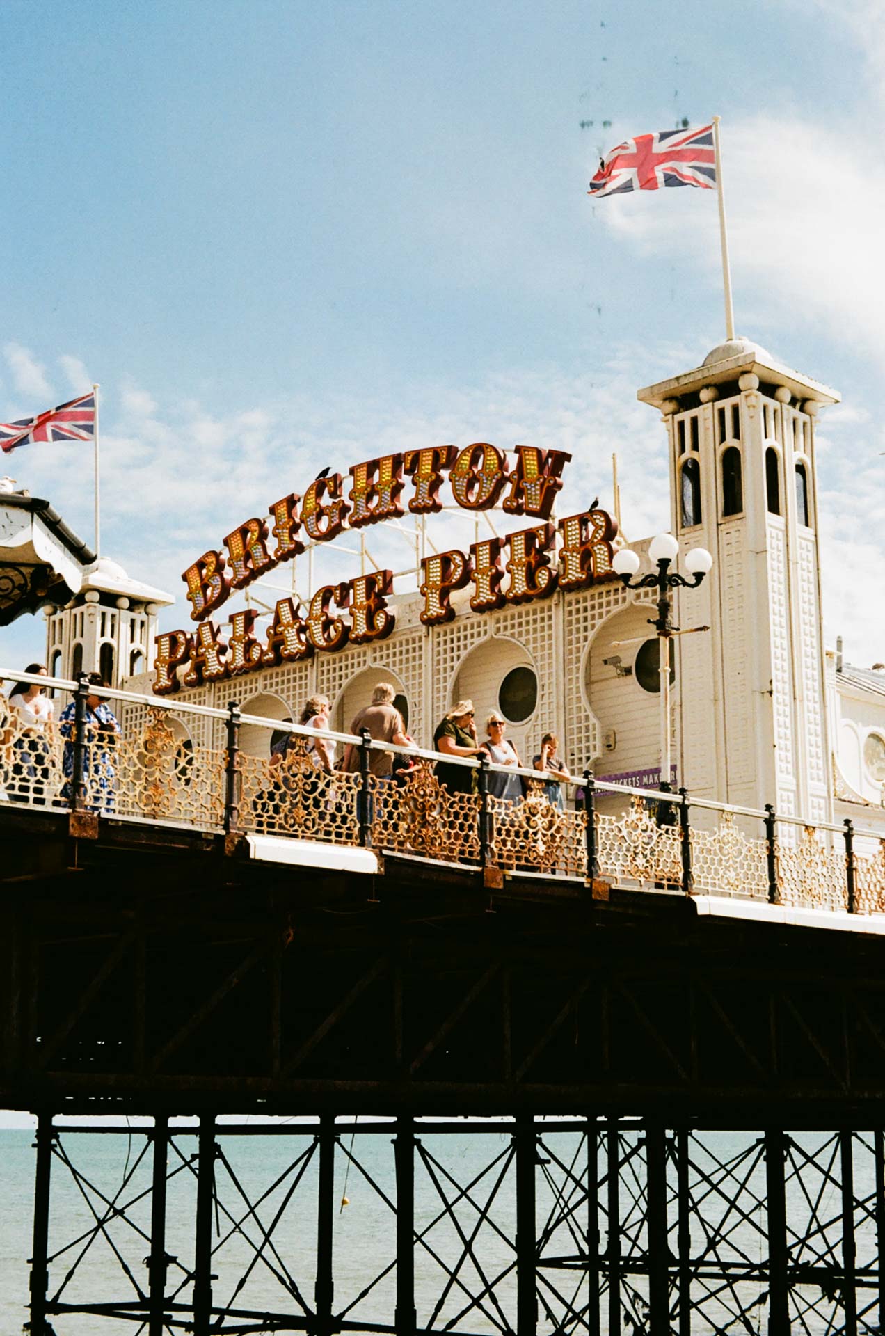 A photograph of Brighton Palace Pier entrance sign with two union jack flags taken on Kodak Gold 200 film stock.