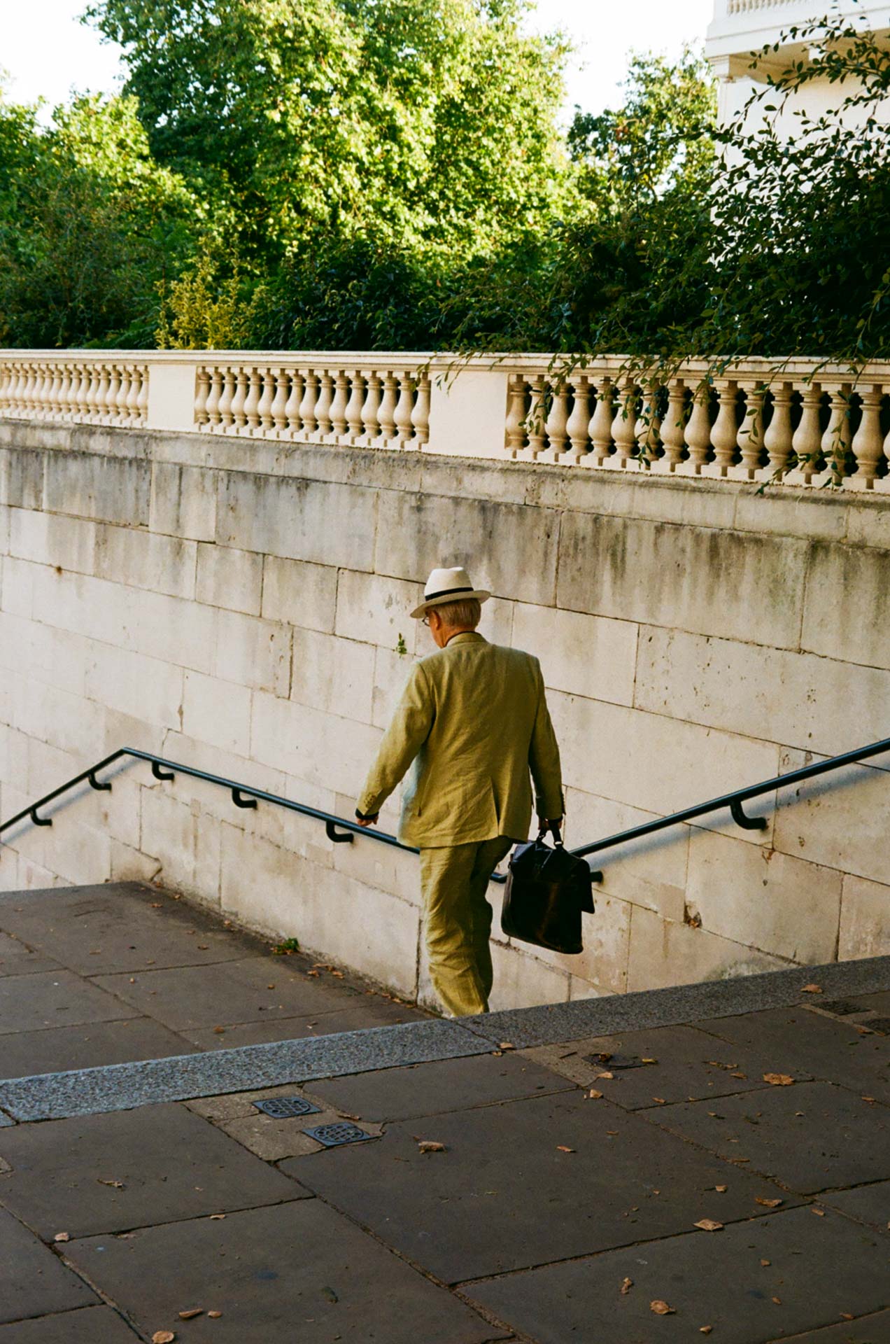 A man in a hat and suit holding a briefcase descends stairs near Whitehall in London. Street photography taken on Kodak Gold 200 film stock.