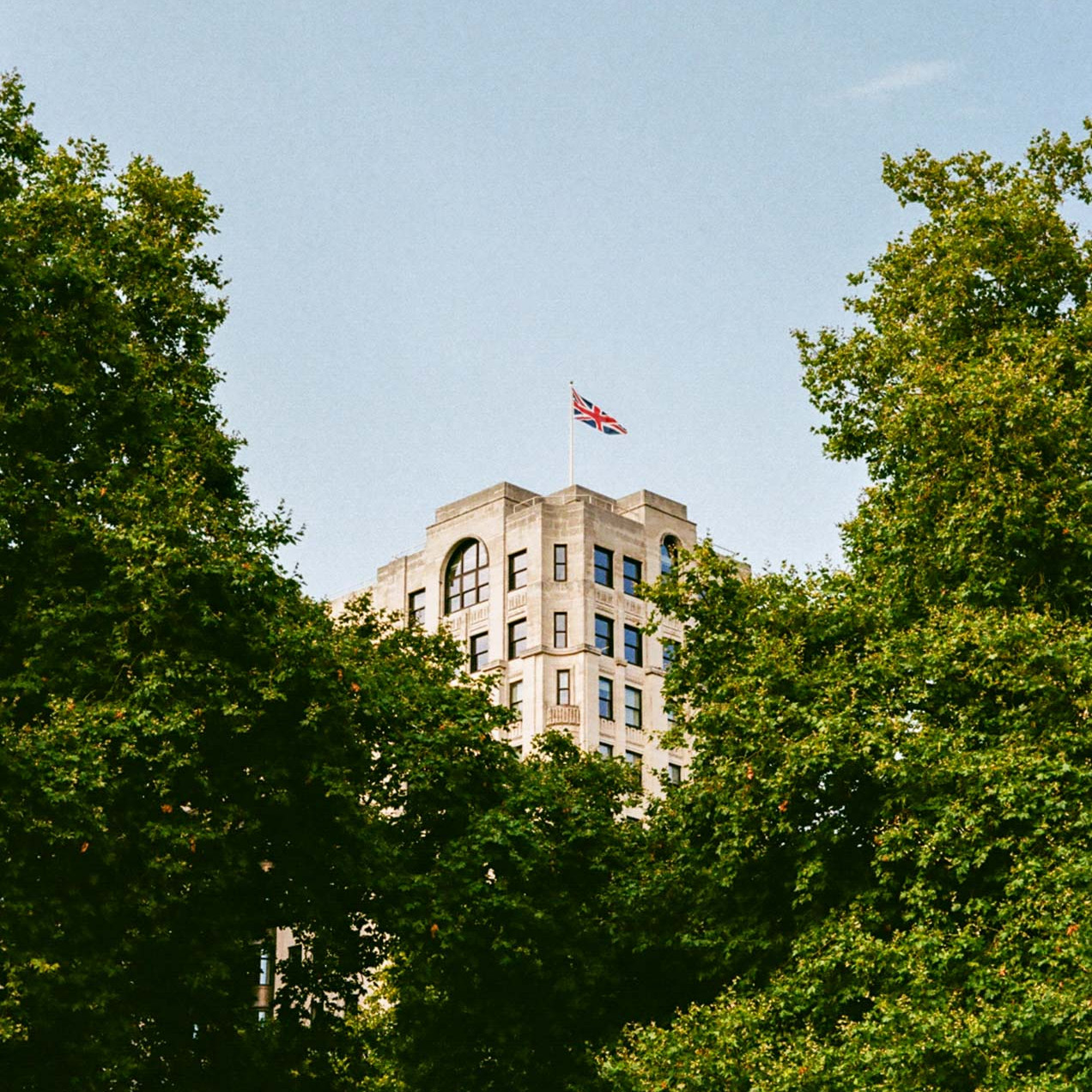 A film photograph of a union jack waving from a London building taken on Kodak Gold 200 film stock.