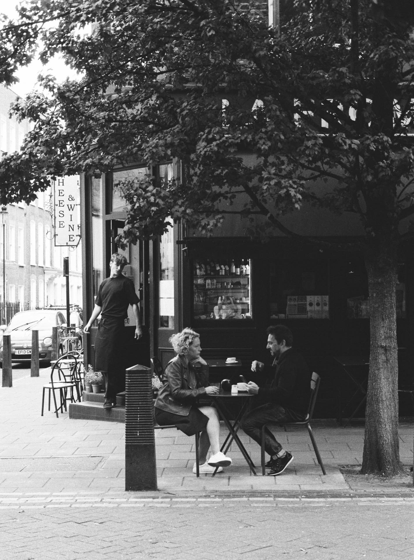Cathy Newman and a friend enjoy a coffee on Lamb's Conduit street, London. Taken on Ilford HP5 Plus film stock.