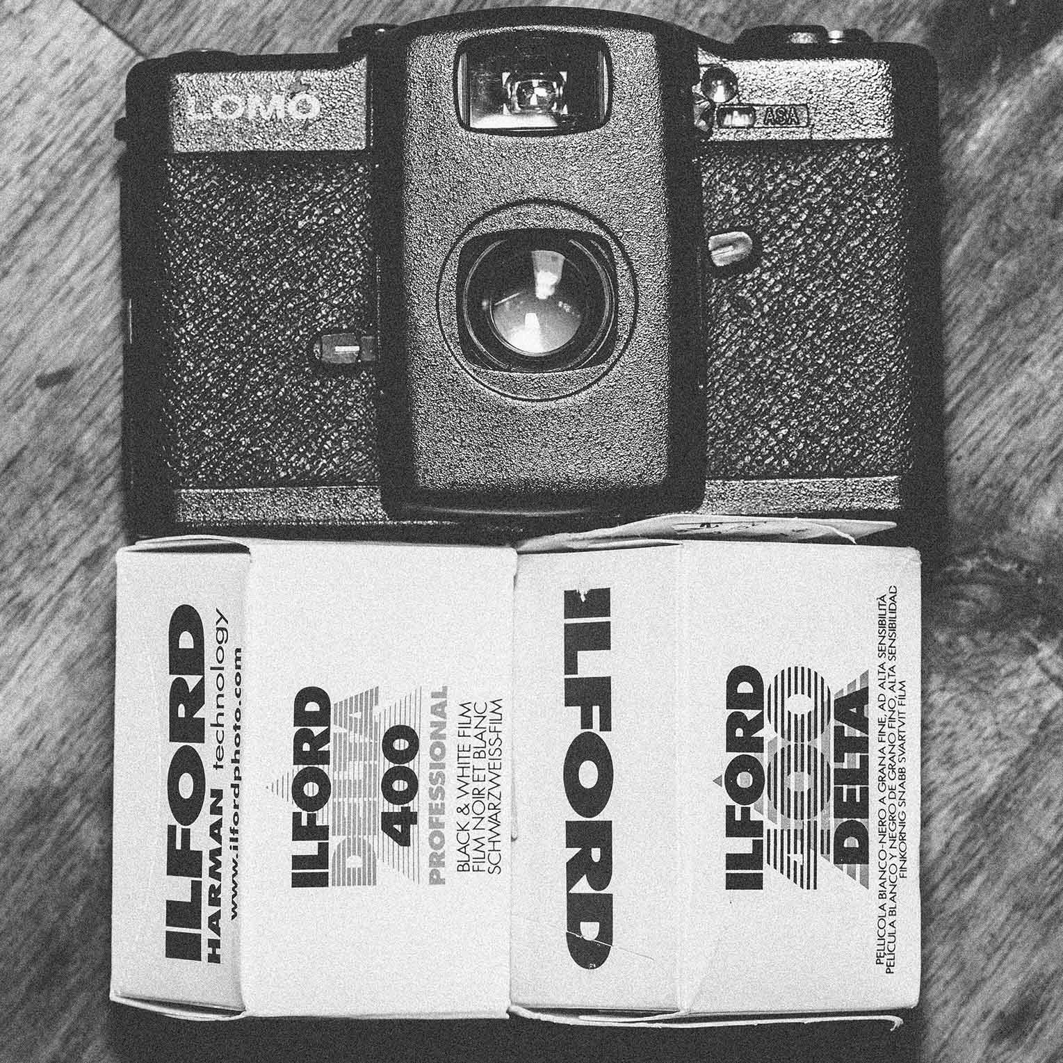 Black Lomo Camera next to two rolls of Ilford Delta 400