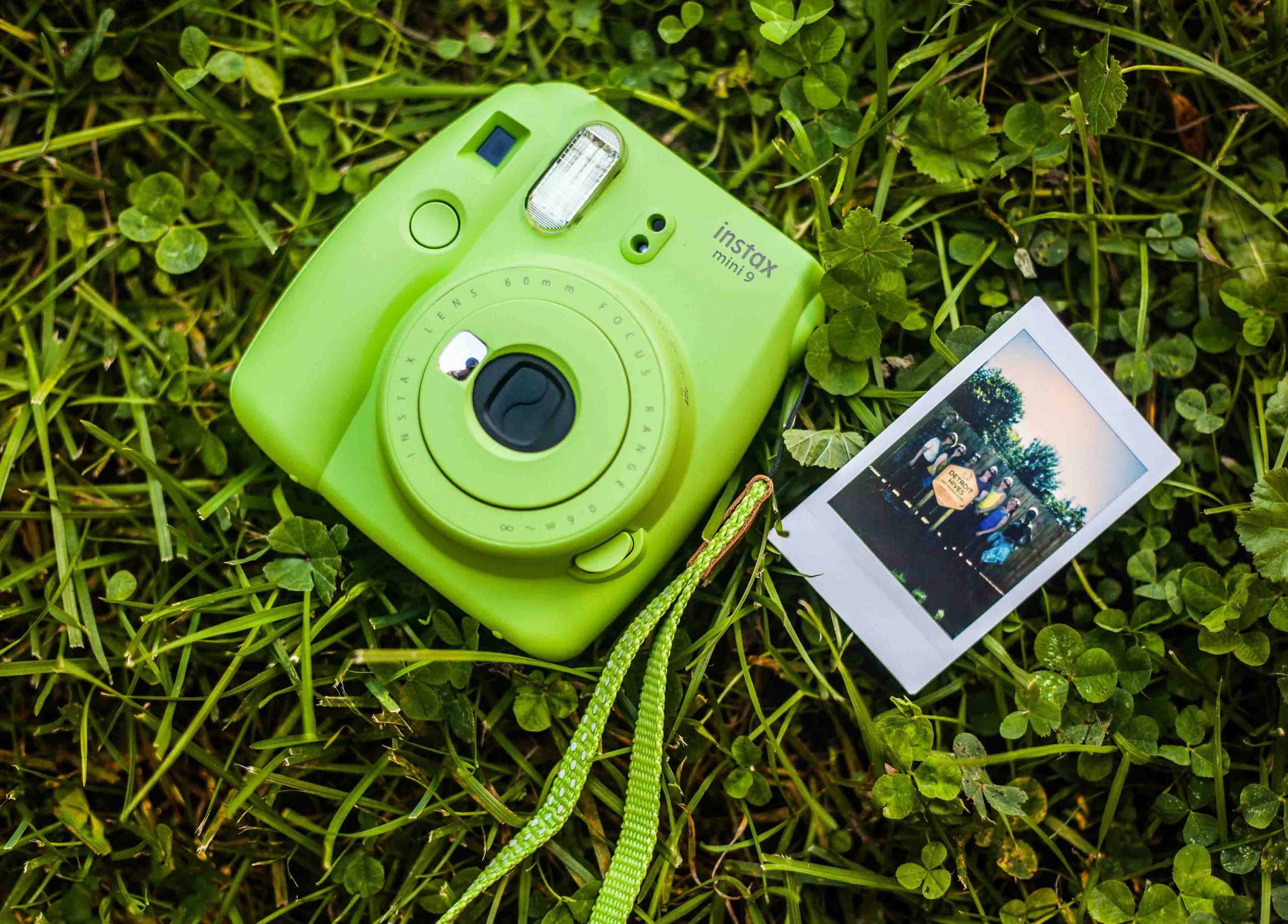 An instax film camera next to a photograph lying on grass.